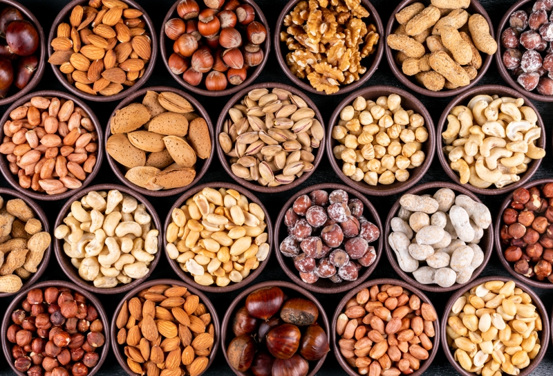 Set of pecan, pistachios, almond, peanut, cashew, pine nuts and lined up assorted nuts and dried fruits in a mini different bowls on a black stone background. flat lay.